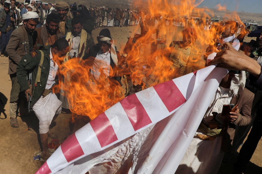 Flames engulf US flag held up in sand 