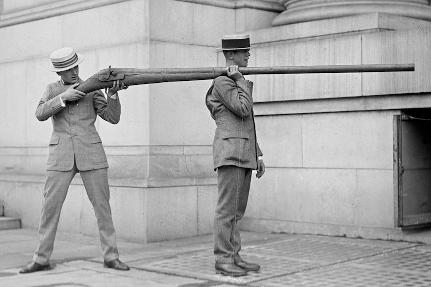 Two men in 1920s America holding a punt gun shoulder to shoulder.