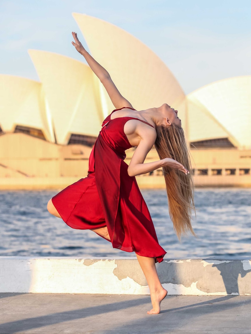 Dancer Cassidy Richardson dances in a red dress with the Sydney Opera House behind her.