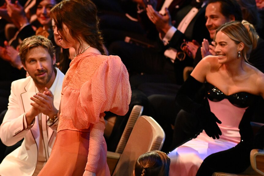 Ryan Gosling winks at Emma Stone as she walks past to accept her BAFTA, as Margot Robbie looks on