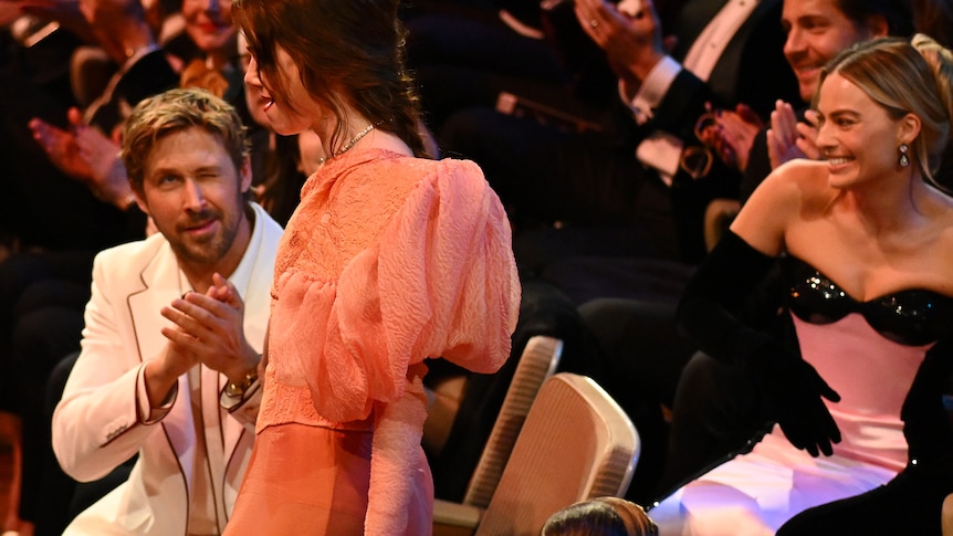 Ryan Gosling winks at Emma Stone as she walks past to accept her BAFTA, as Margot Robbie looks on