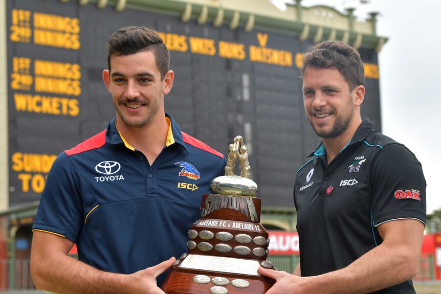 Port Adelaide captain Travis Boak (on the right) and Adelaide captain Taylor Walker (left of photo) hold a trophy.