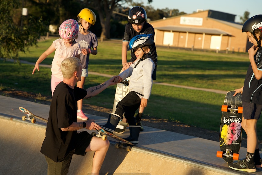 Jayden Sheridan stands on the skateramp, teaching a group of kids how to skate.