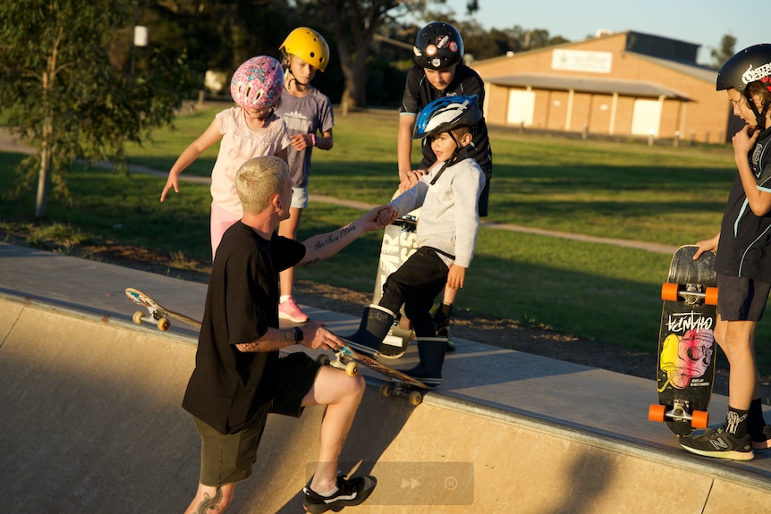 Jayden Sheridan stands on the skateramp, teaching a group of kids how to skate.