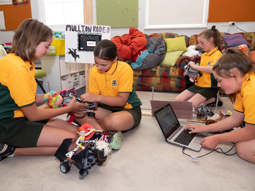 Four female students inspecting small robots in classroom.