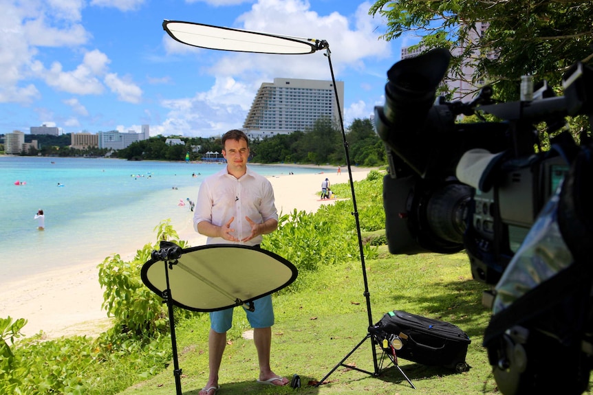 Andrew Greene standing under reflector boards in front of TV camera on beach in Guam.