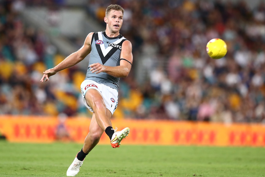 An AFL player looks up as he follows through after kicking the ball downfield during a game.