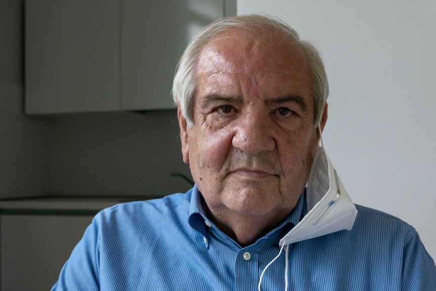 Vando Fossati wears a blue shirt, a surgical mask hangs from his ear.