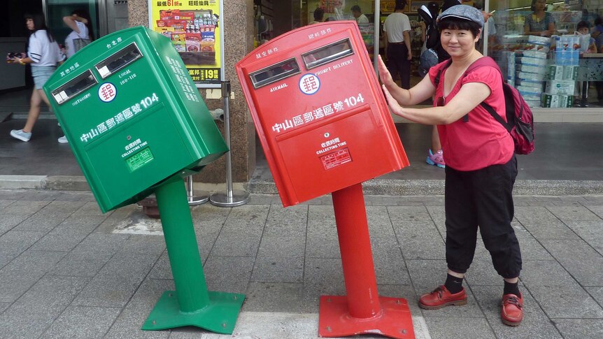 Woman stands next to two mailboxes bent out of shape by strong winds from Typhoon Soudelor in Taiwan