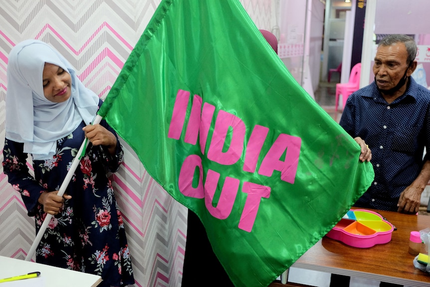woman poses with green flag that says "india out" in bold pink letters