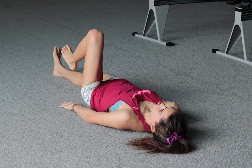 Ella Cummings lying on her back on the floor of a gym flexing her left knee
