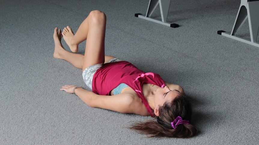 Ella Cummings lying on her back on the floor of a gym flexing her left knee