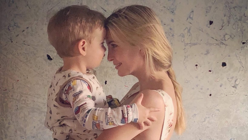 Side view of Ivanka Trump holding her young son, son wearing pyjamas, mother and son's foreheads pressed together, smiling