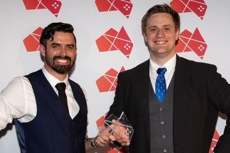 Two men hold and award and smile broadly