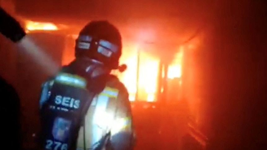A firefighter in front of a room on fire. 