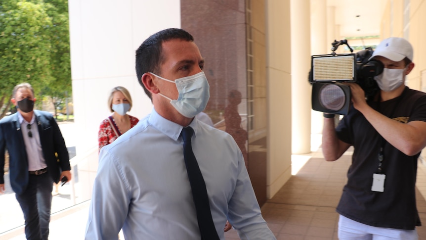 A man in a suit and a face mask walks into court. 