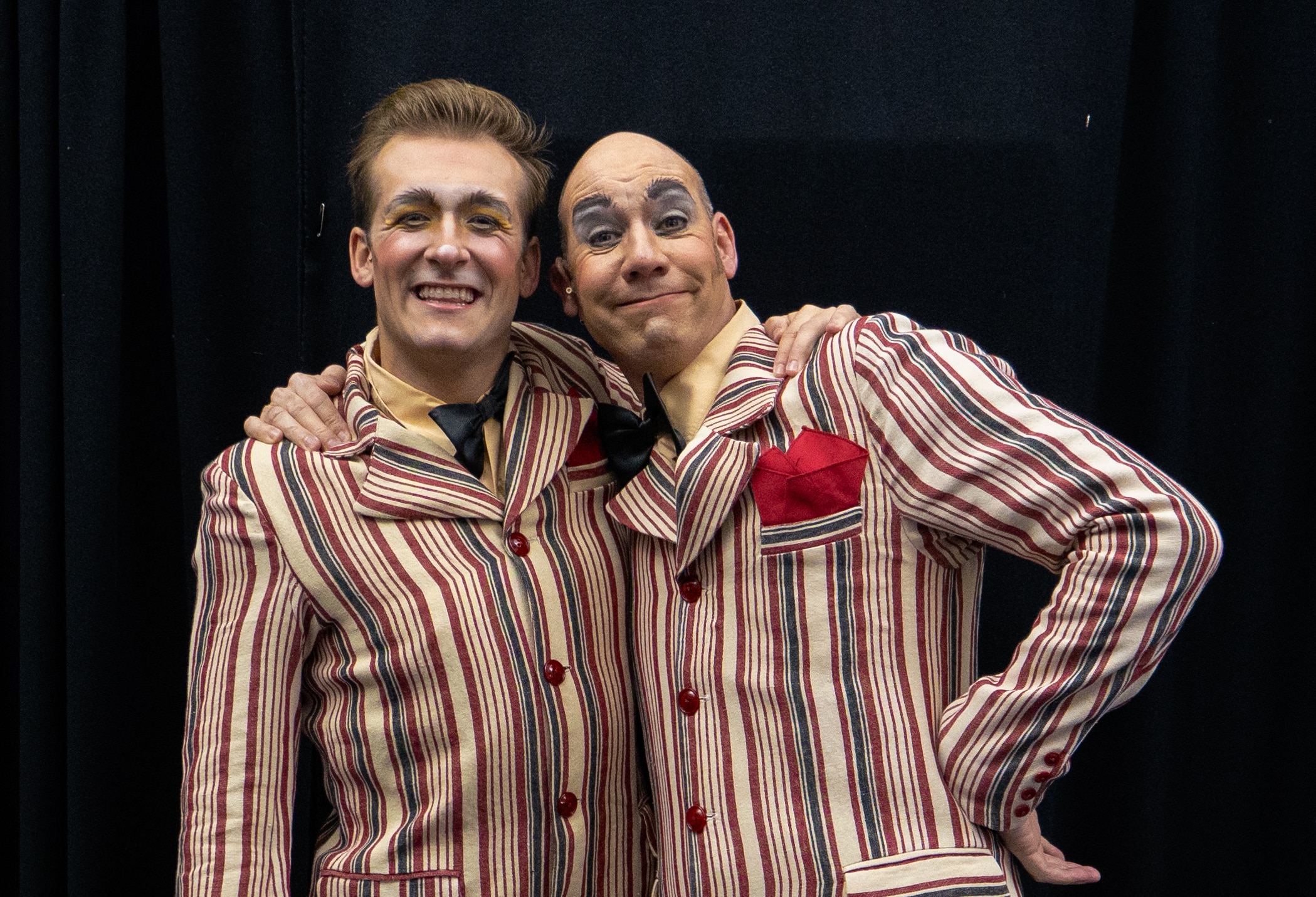 Two men, one young, in stripy shirts in red, white and black with clown make up.