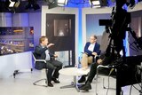Radio Free Europe broadcast from their Moscow TV studio. Two men and another person speak on the set as the crew film them.