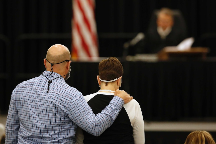 Two people hug while wearing face masks to protect against coronavirus.