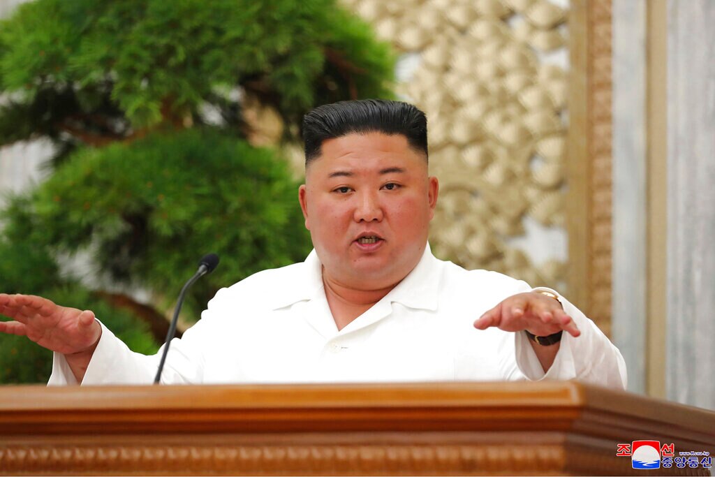 Kim Jong Un gestures at a lectern wearing a white shirt.