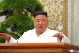 Kim Jong Un gestures at a lectern wearing a white shirt.