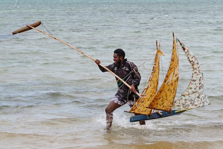 Man with model boat walks through the water.