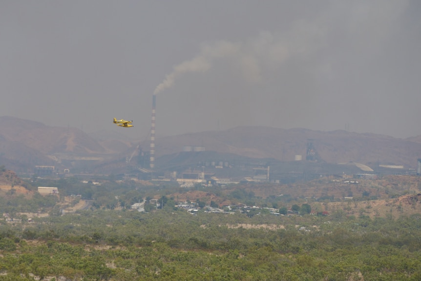 A water bomber with smokey mining city in the background