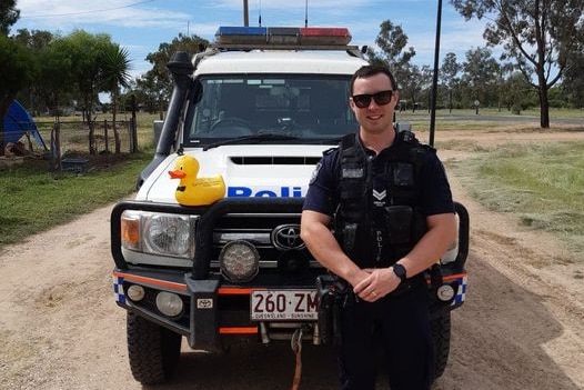 A police officer poses with a yellow rubber duck on the bullbar of his car