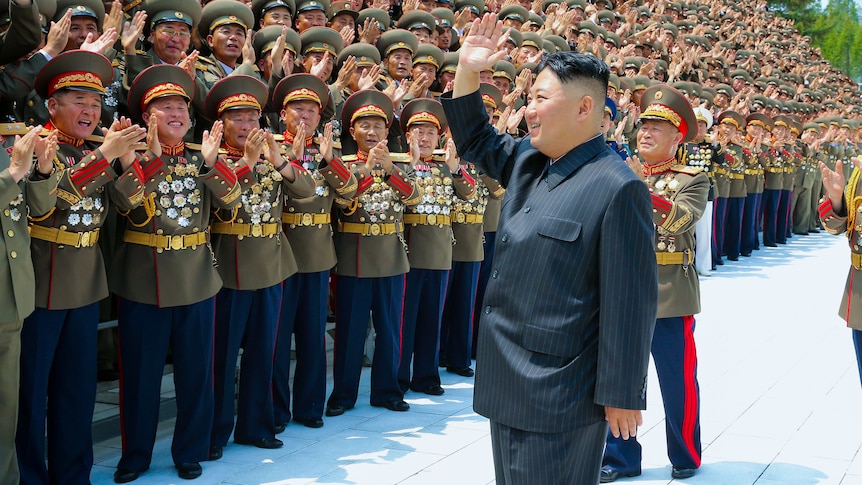 Kim Jong Un waves to a group of men in North Korean military dress uniforms