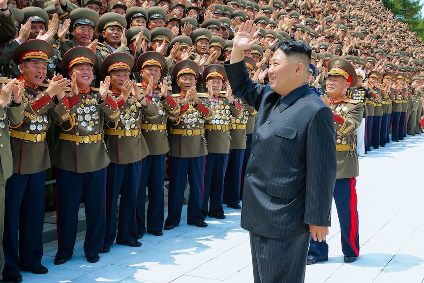 Kim Jong Un waves to a group of men in North Korean military dress uniforms