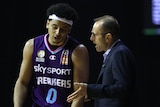 A basketball player looks down as his coach gestures and talks to him during a game.