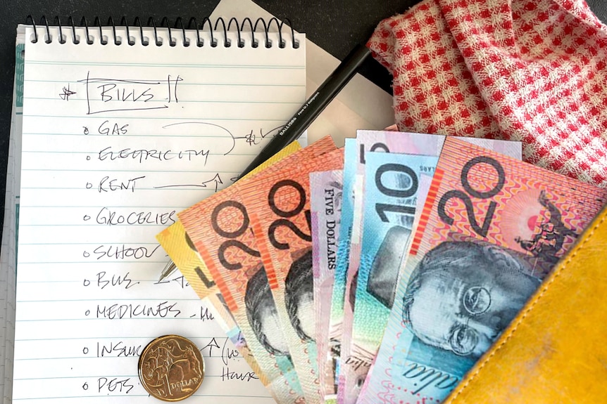 Cash lays on a kitchen table beside a cup of tea and a list of bills owing 