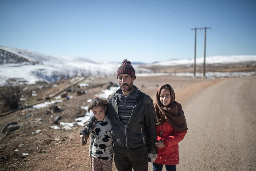 A man and his daughters pose for a photo with a wide snowy landscape behind them.