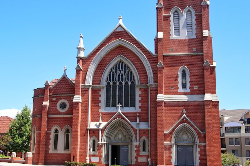 An exterior picture of a large brick Catholic Church with leadlight windows and white trim.