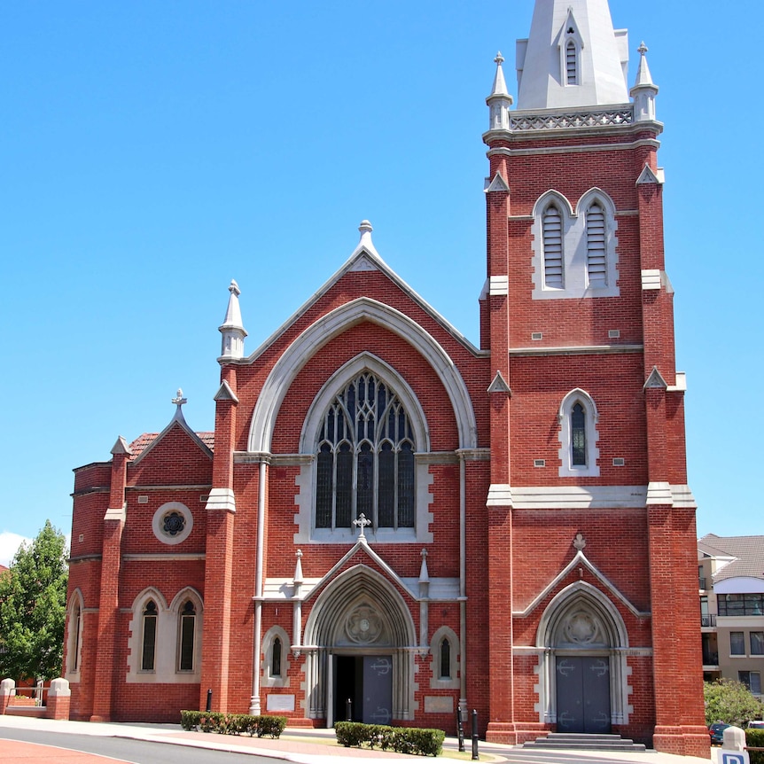An exterior picture of a large brick Catholic Church with leadlight windows and white trim.