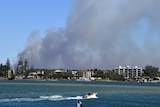 Dark smoke from bushfires is seen as it approaches Caloundra on a backdrop of blue skies and clear water at the beach.