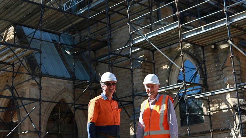Kent and David wear hard hats and high vis in front of St Paul's Cathedral surrounded by scaffolding