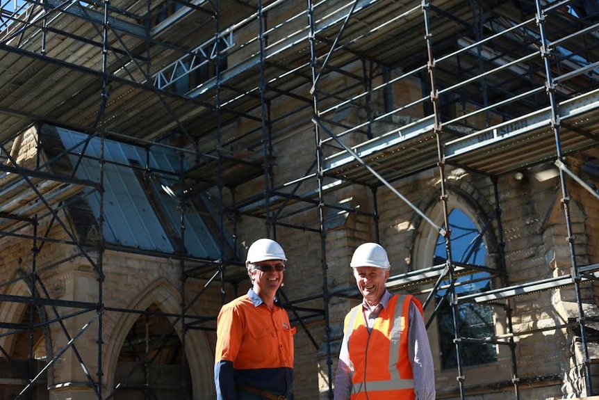 Kent and David wear hard hats and high vis in front of St Paul's Cathedral surrounded by scaffolding