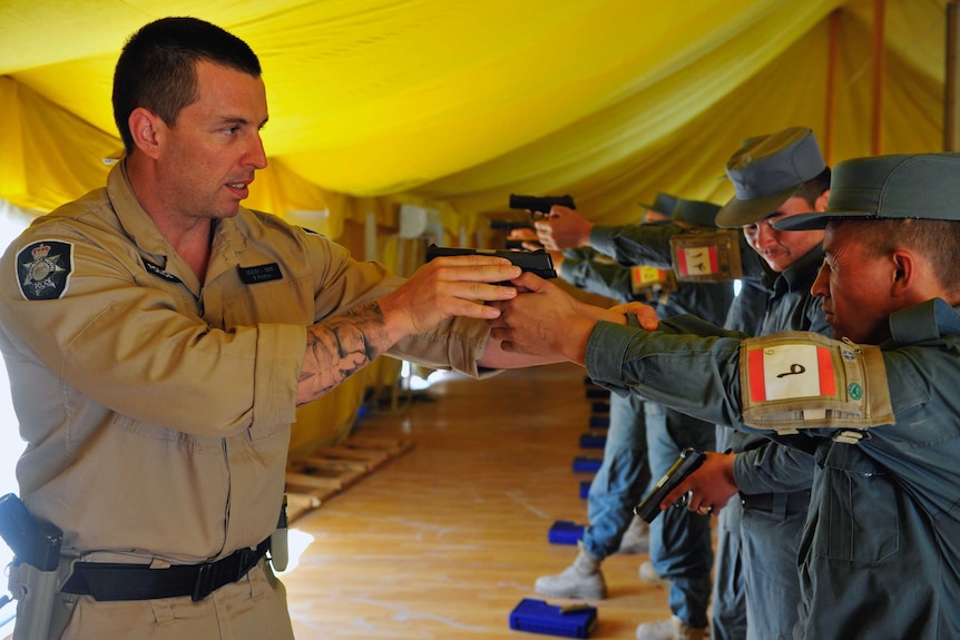 A man shows a group of other men in military uniform how to disarm someone with a pistol.