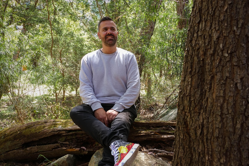 a man in Aboriginal flag shoes sits on a fallen log in the grampians forest