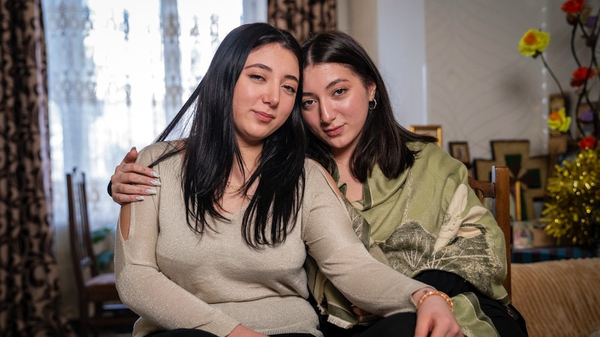 Identical twins sitting on a sofa, smiling at the camera and embracing