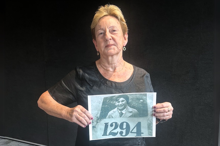 A woman holds a photograph of a boy in a collared shirt. There's a tag underneath the photograph with the number "1294".