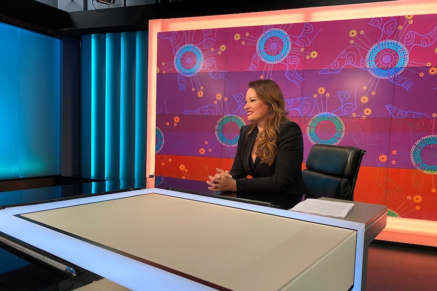 Larissa Behrendt smiles while she is sitting down on a chair in a TV studio