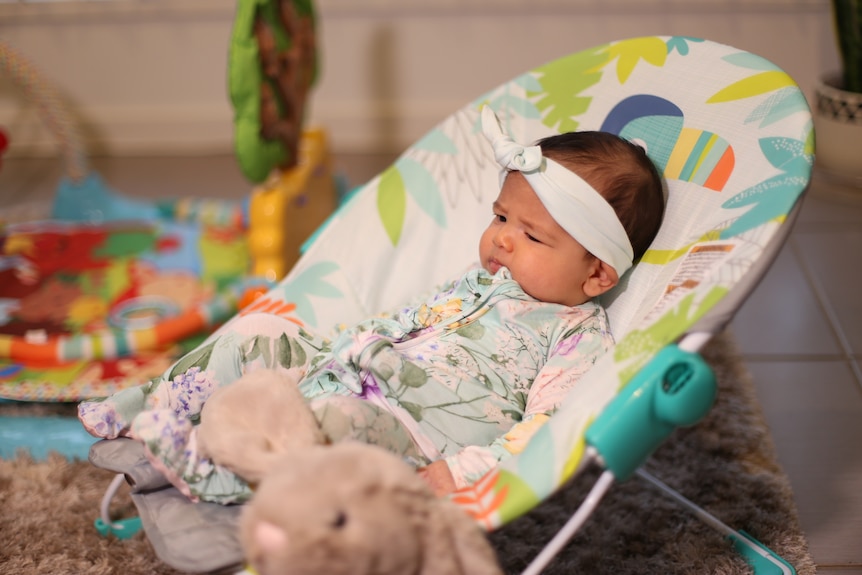 A baby sits in a chair surrounded by toys
