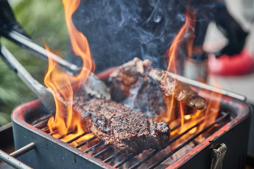 Beef being cooked on a flaming grill.