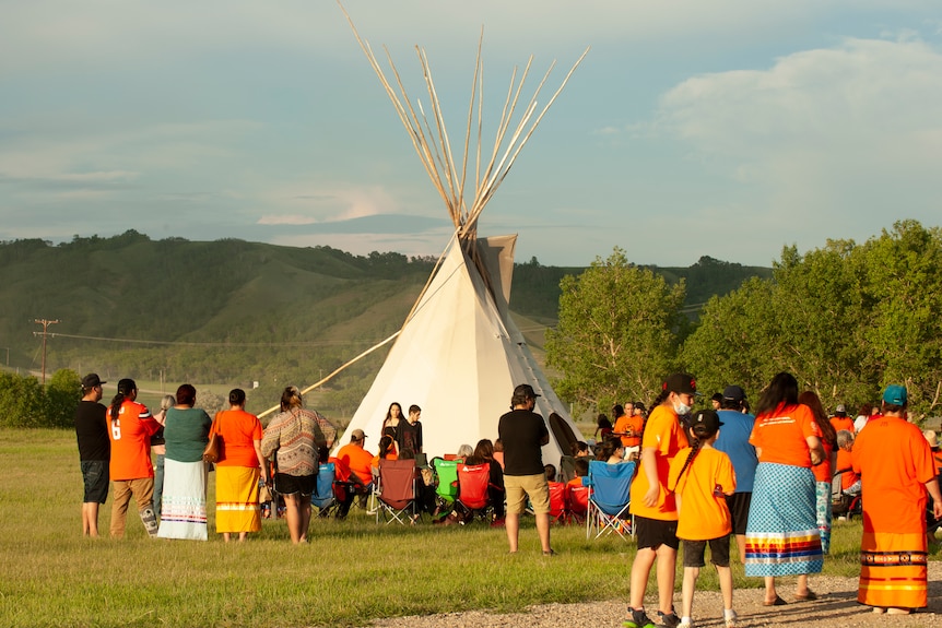 A tepee and Indigenous groups are seen holding a vigil at the site of the unmarked graves