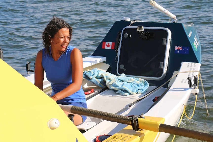 A woman in a blue top sits in a yellow rowing boat.