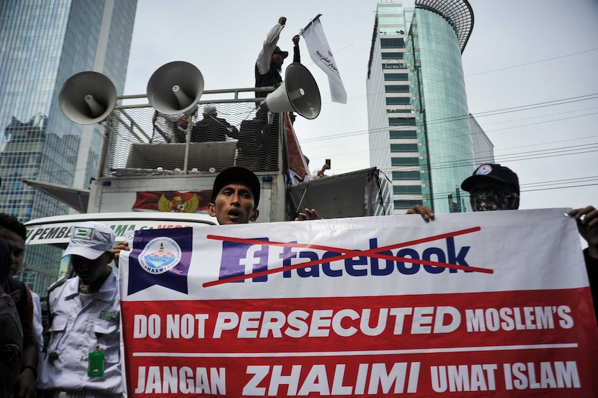 A demonstrator holds a banner with Facebook logo crossed out