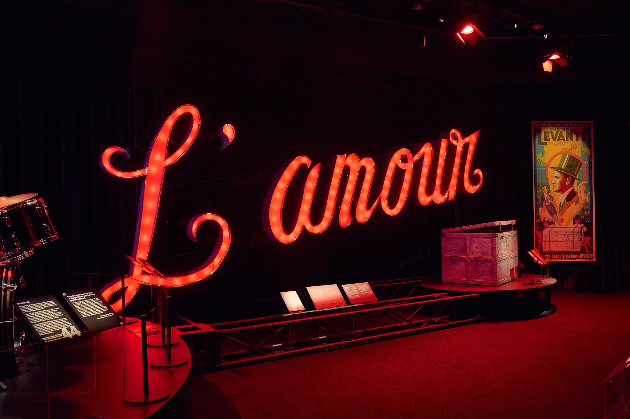 A red neon sign says "L'amour" in cursive writing and sits with other props.