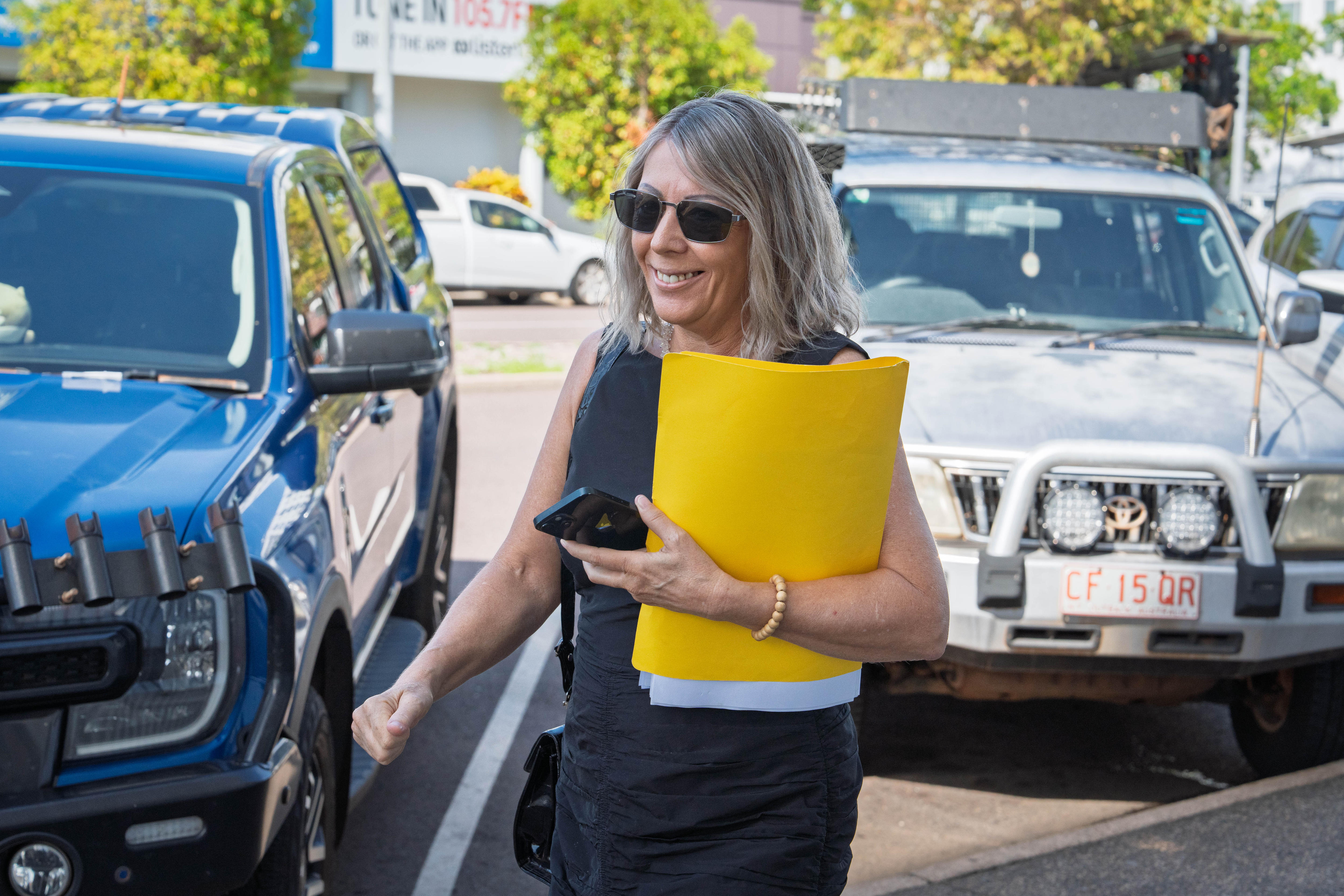 Una mujer sonríe al entrar al Tribunal de Magistrados de Darwin sosteniendo una carpeta amarilla.
